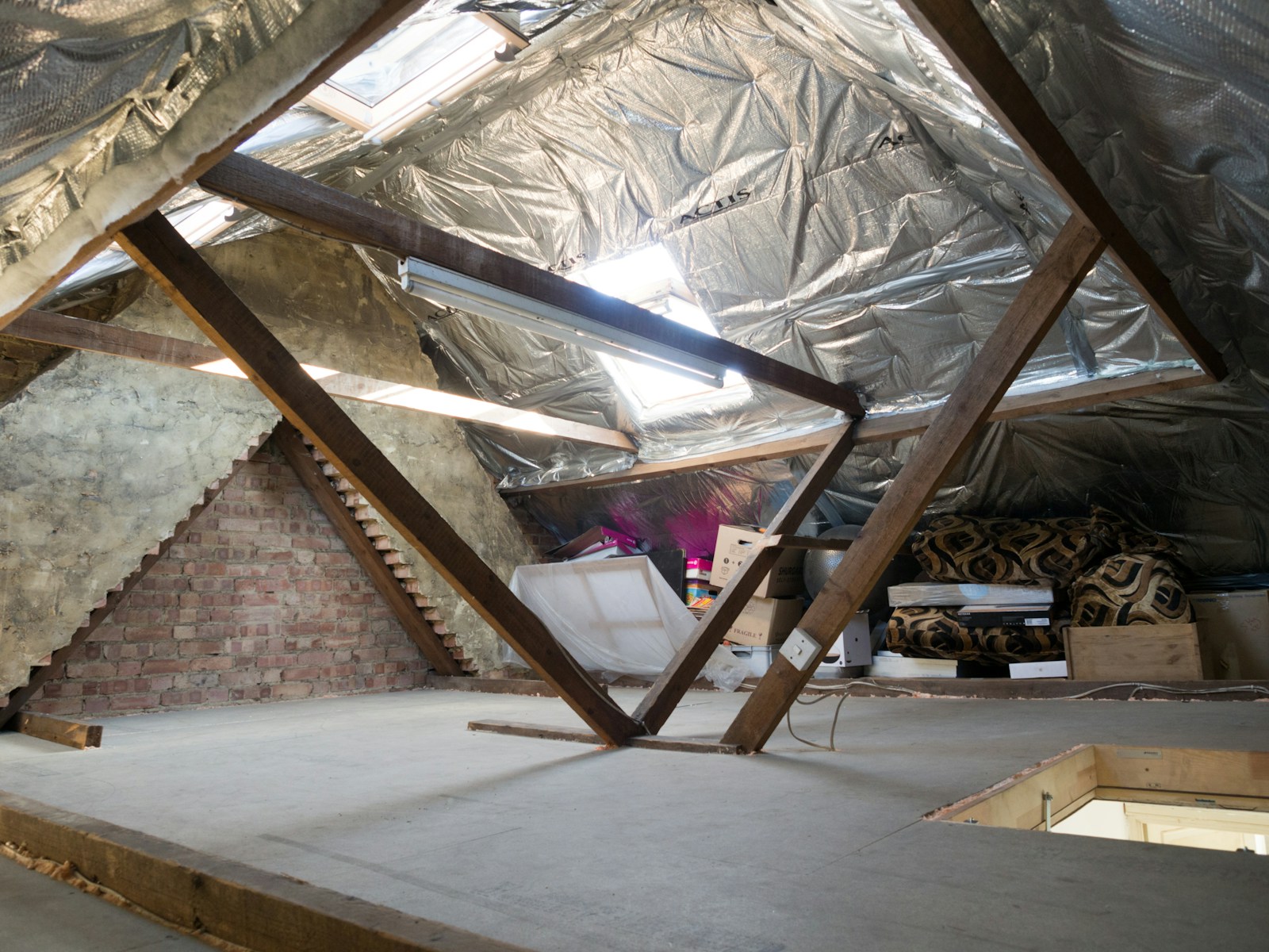 An attic with timber beams, insulation and an access opening